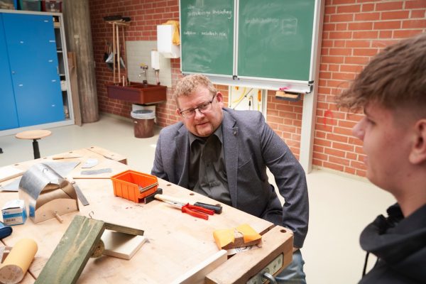 Bernd Wölbern (links) sitzt an einer Werkbank und tauscht sich mit einem Schüler über die Angebote des Zevener Bildungsweges aus.